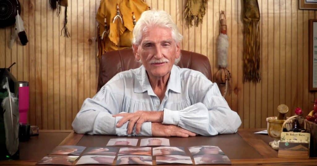 Dr. Morse in white shirt sits at desk with photos displayed, Native American decor on wood-paneled walls